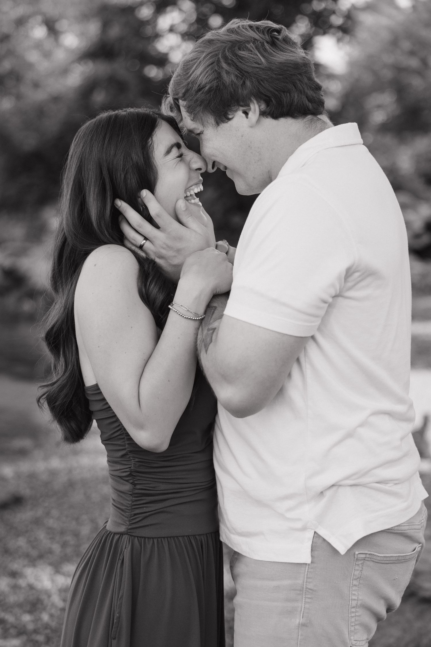 Black and white photo of a laughing couple sharing a tender moment with the mans hand on her face.