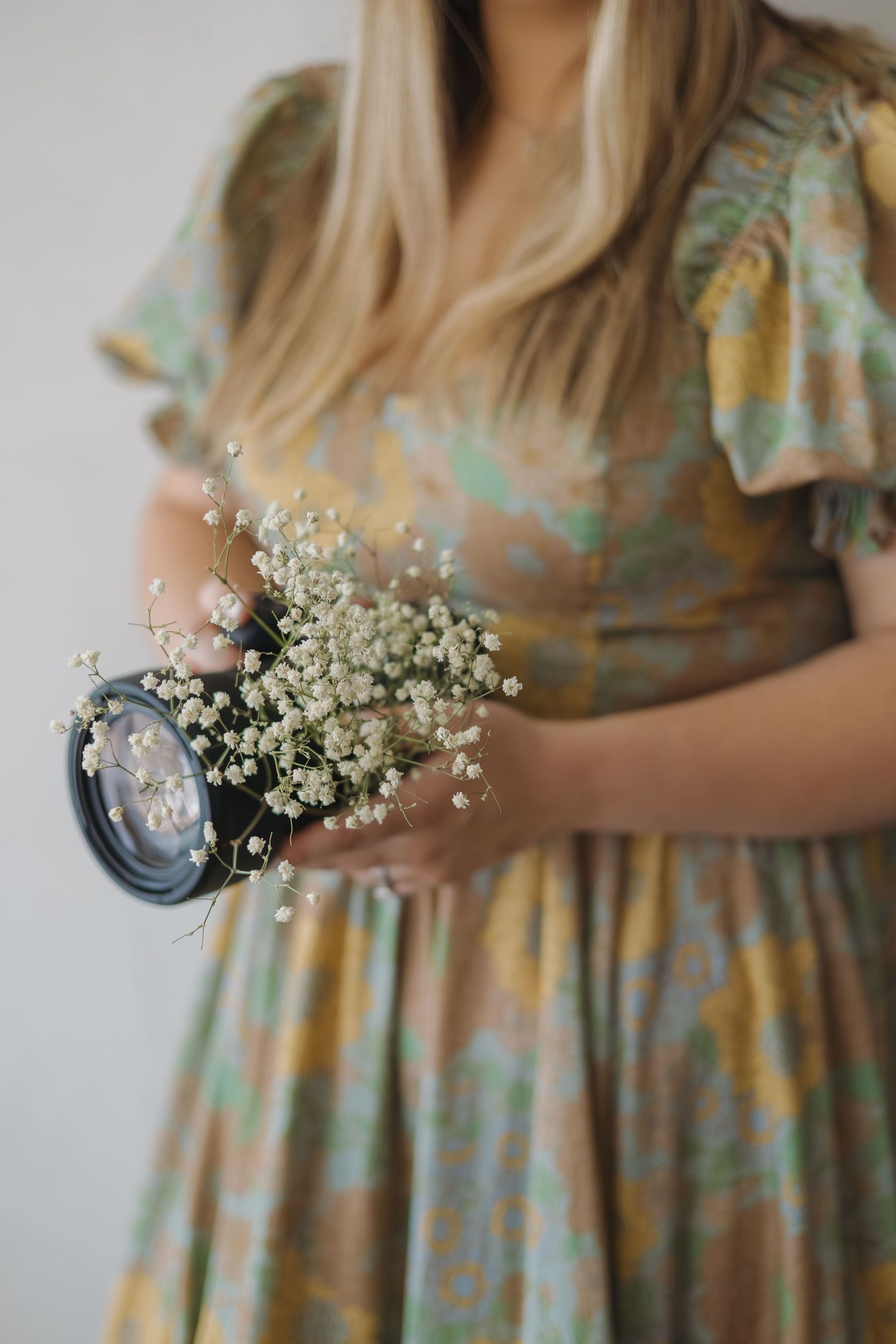 Close-up of woman in floral dress holding a camera lens with delicate white baby's breath flowers.