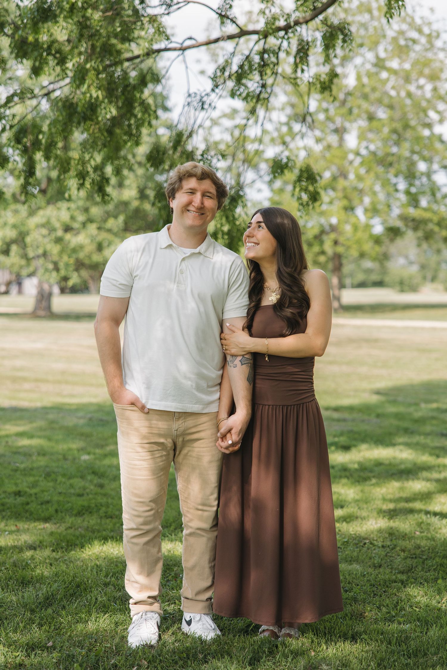Smiling couple holding hands and standing close together in a lush green park.