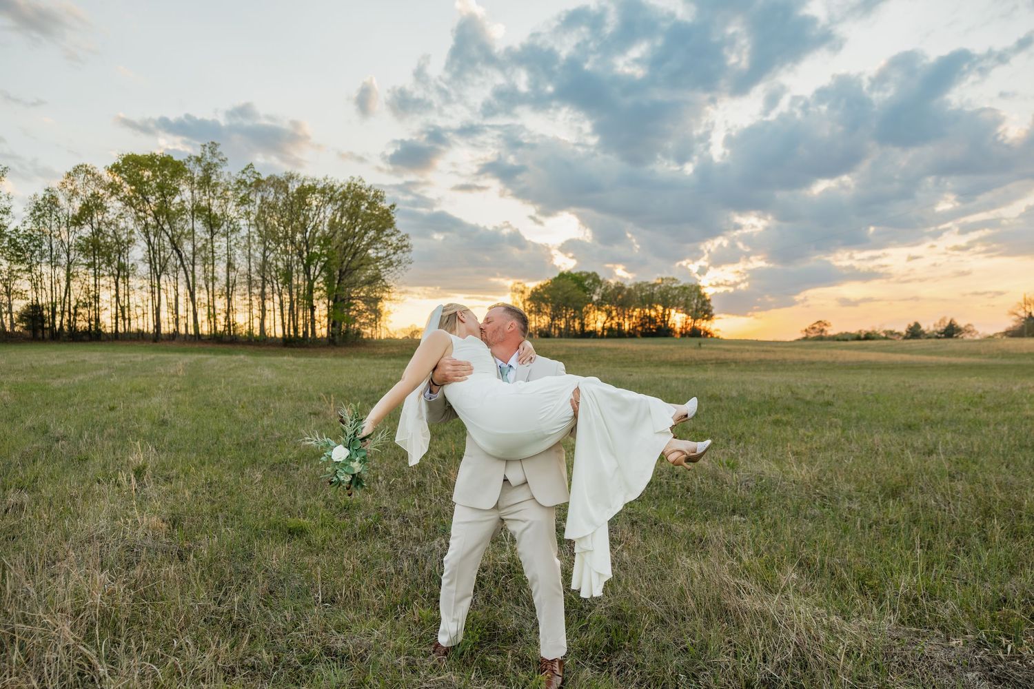 Groom dips bride in a romantic pose in a sunlit field at golden hour.