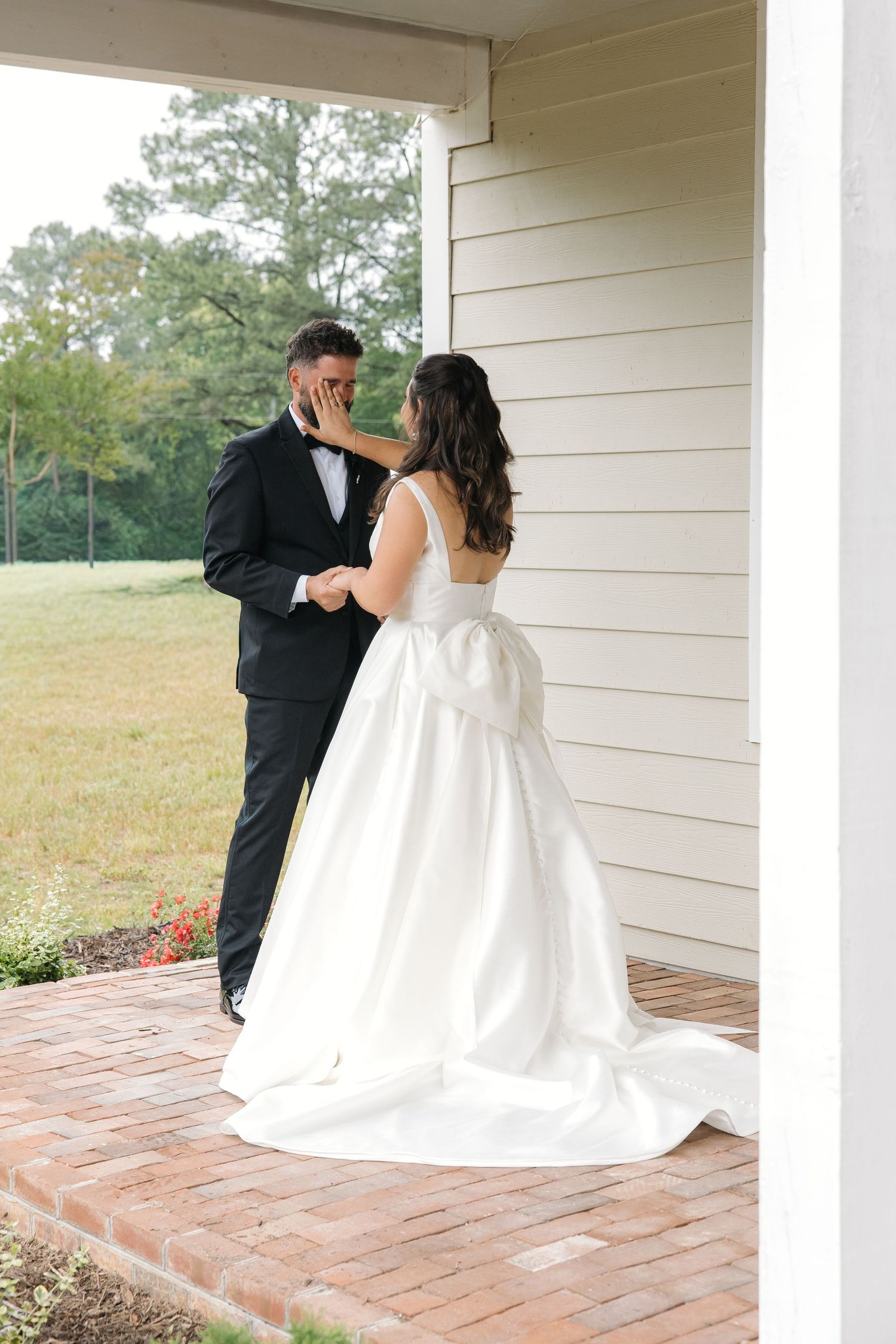 Bride tenderly touches grooms face during an intimate first look moment on a porch.