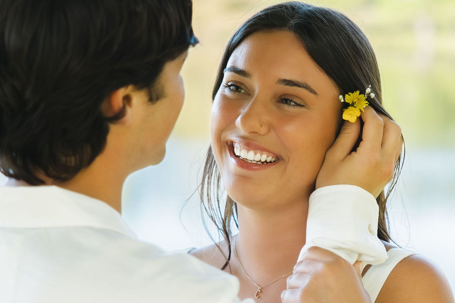 Man tenderly placing a yellow flower in smiling woman's dark hair in a close romantic outdoor moment.