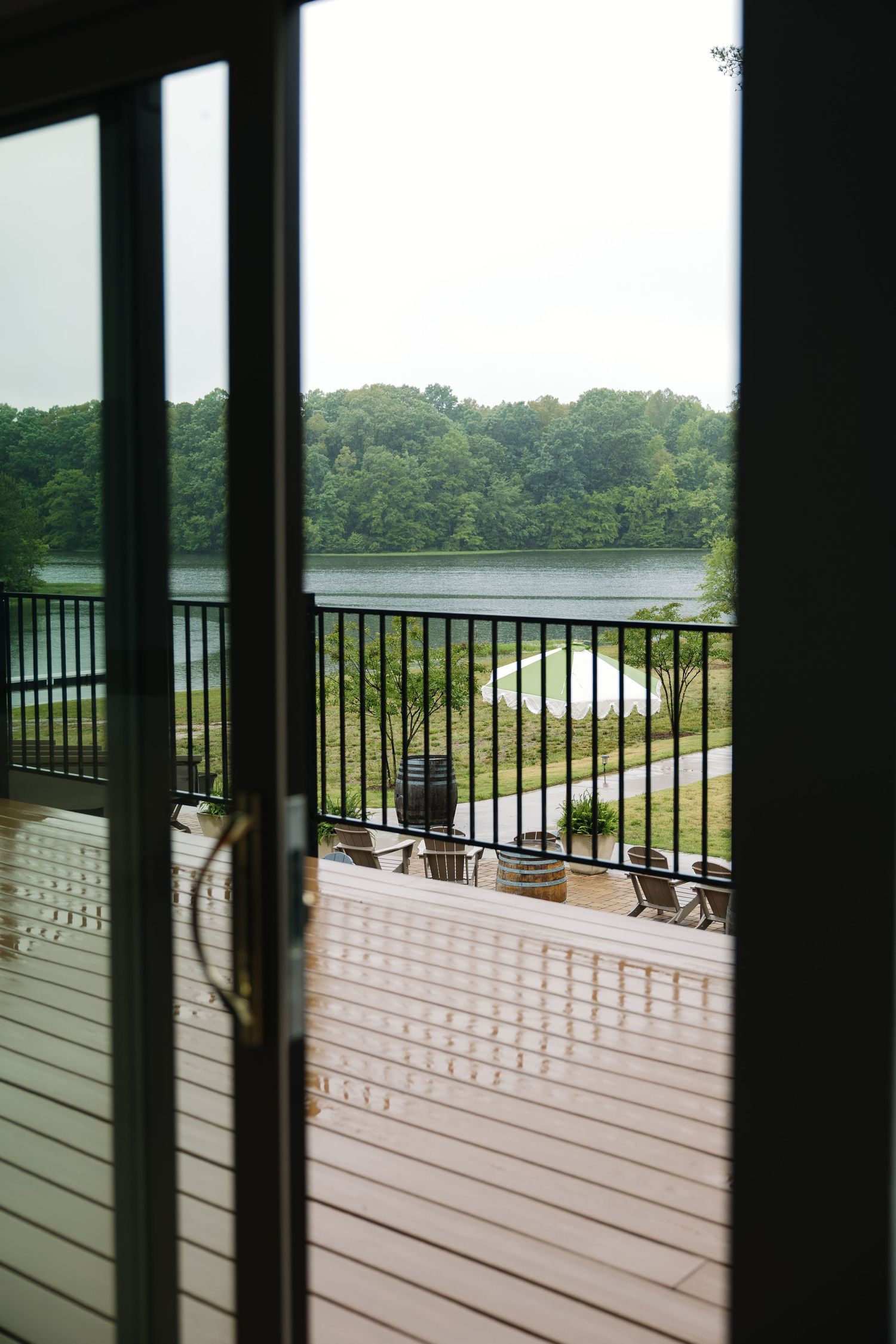 Scenic lakeside view through glass French doors opening to a deck with Adirondack chairs and lush greenery.