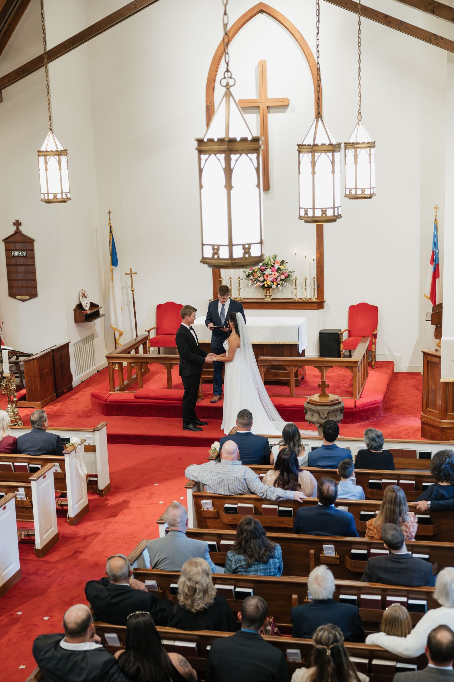 Overhead view of wedding ceremony at church altar with red carpet, cross, and guests in wooden pews.