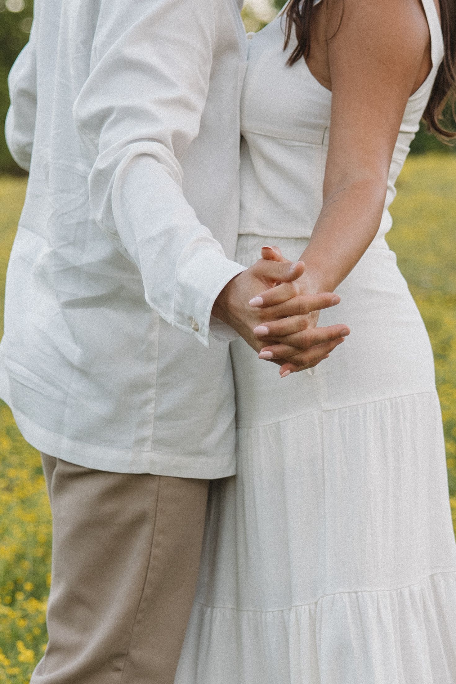 A close-up of a couple holding hands, both dressed in white, standing together outdoors.