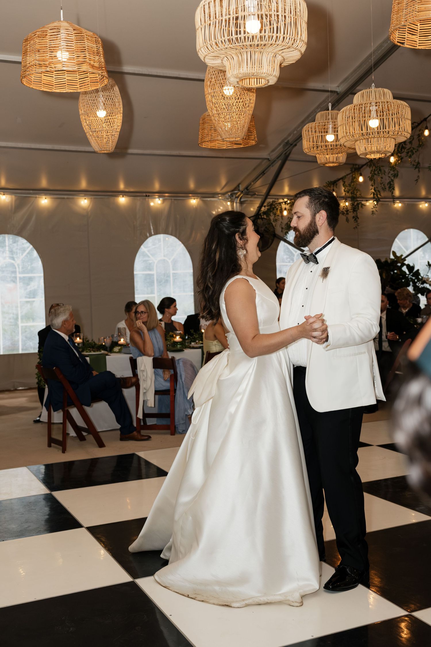 Newlyweds share romantic first dance under warm wicker pendant lights in elegant tented reception.