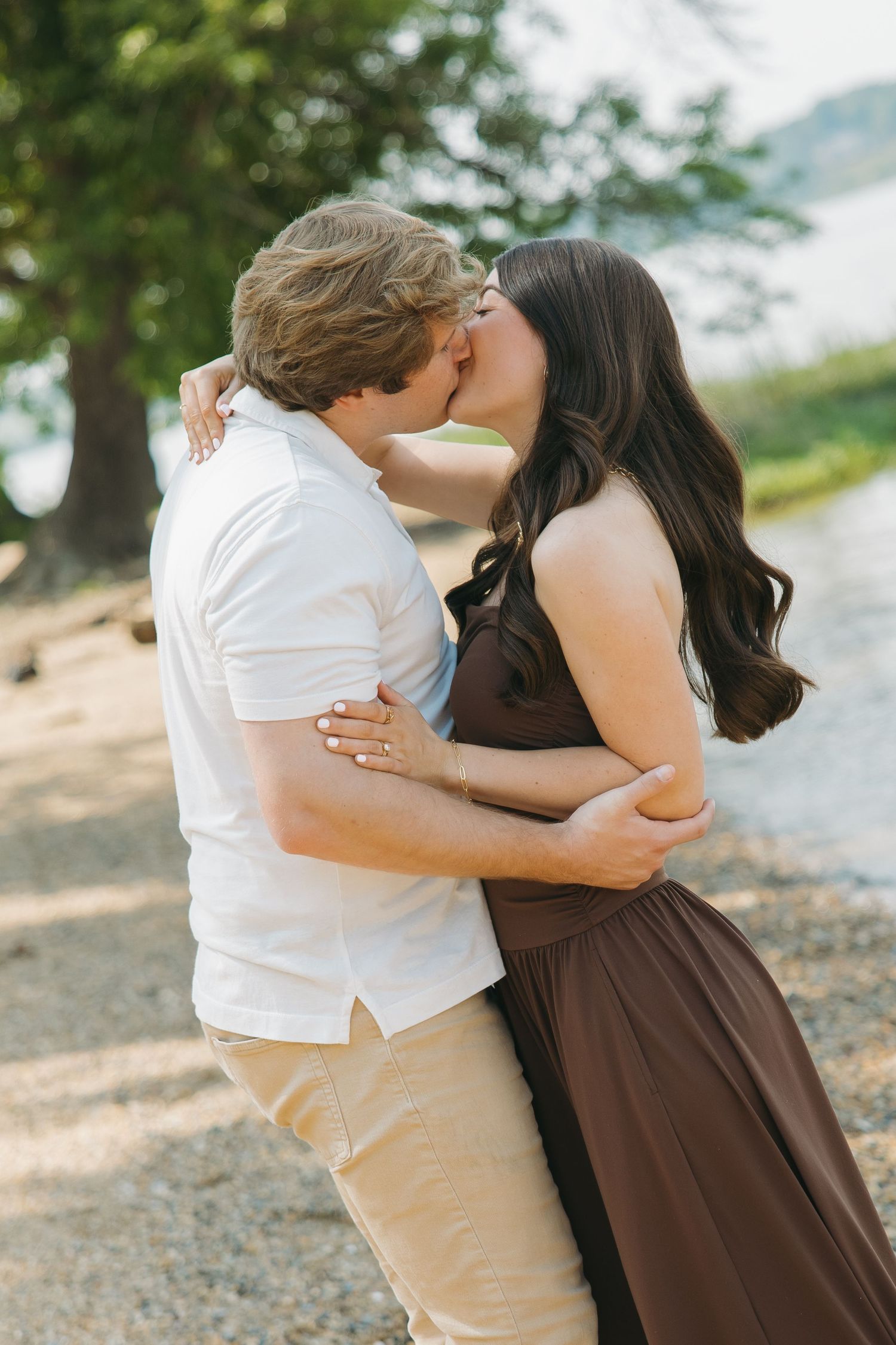 Couple sharing a romantic kiss on a sunny pebble beach by the lake.