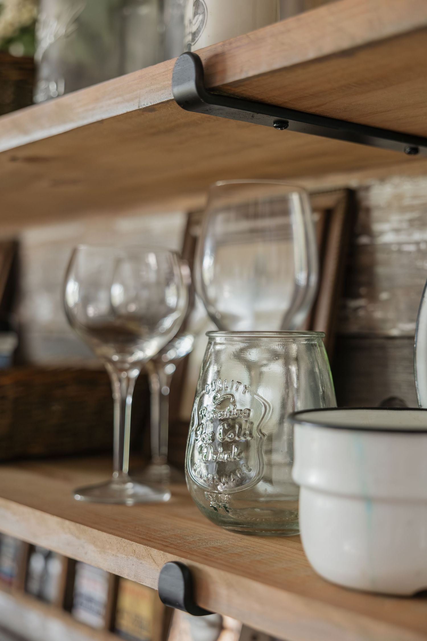 Rustic wooden shelves displaying wine glasses, mason jar, and white ceramic mugs.