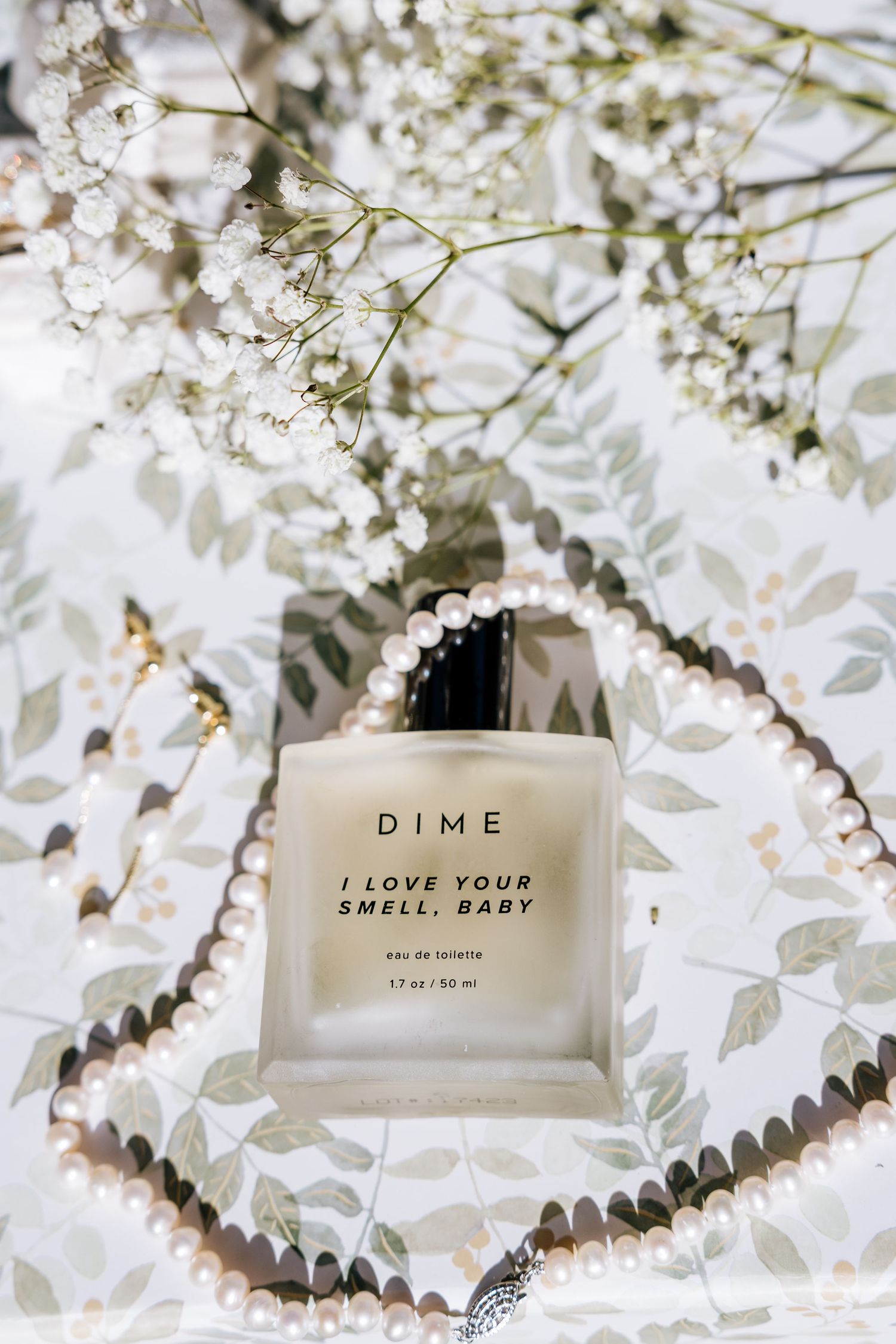 DIME I Love Your Smell Baby eau de toilette perfume bottle surrounded by pearls and white flowers.