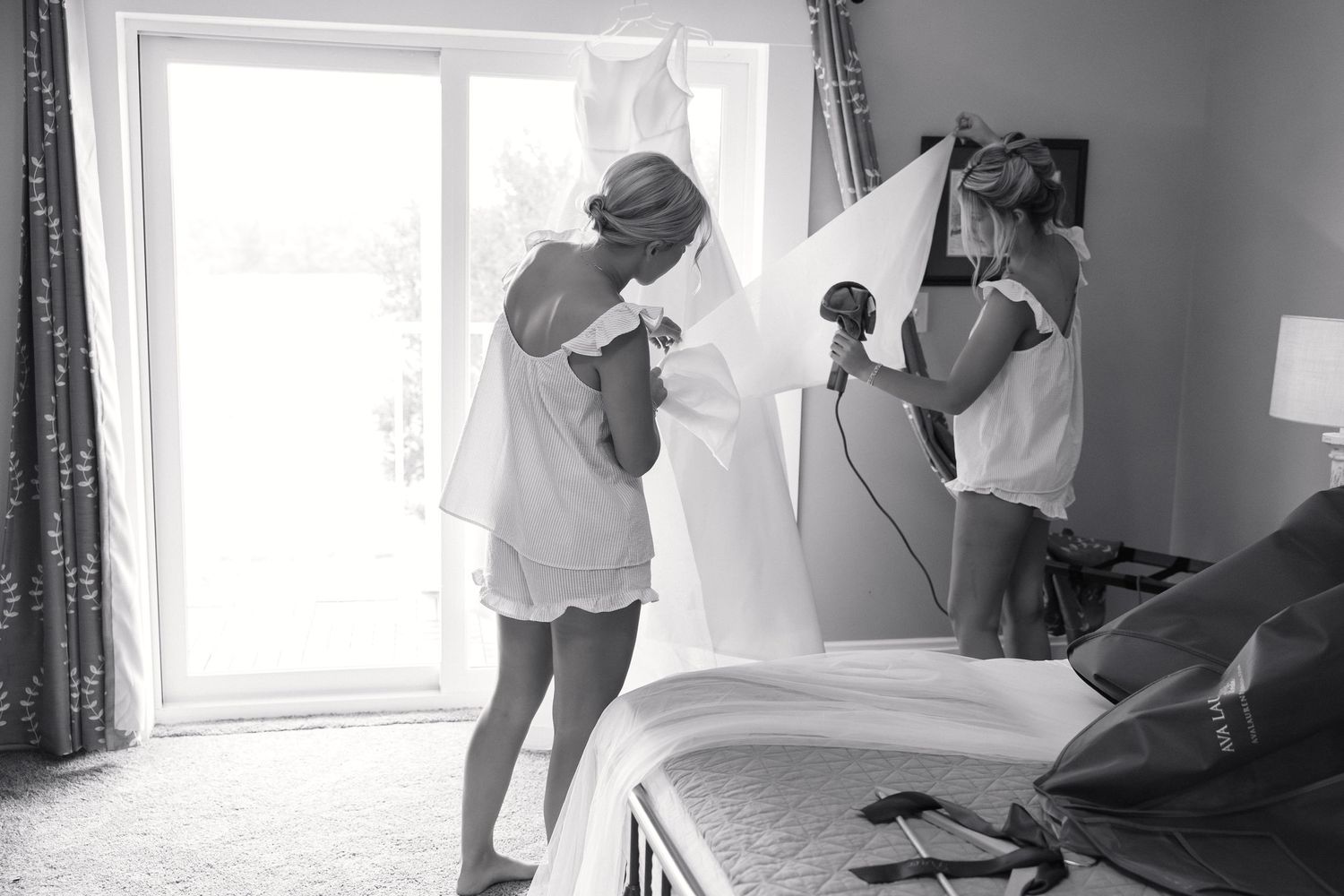Black and white photo of bride getting wedding dress steamed in hotel room on wedding day.