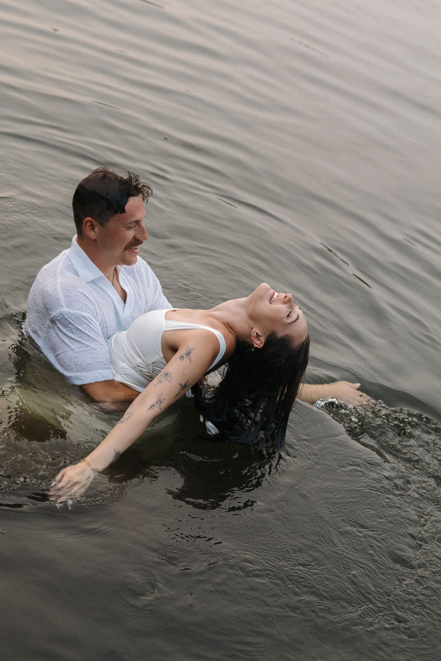 A man and woman standing waist-deep in water, with the woman leaning back joyfully during a baptism ceremony.