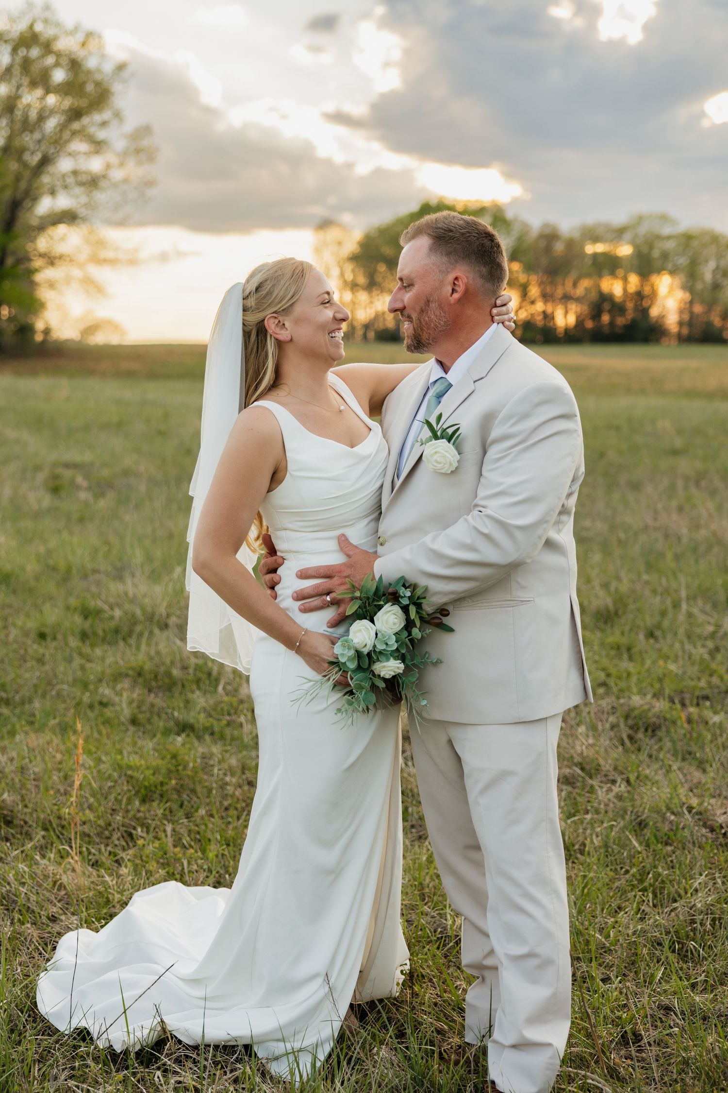 Smiling bride and groom embrace in an open field at golden hour during their outdoor wedding.