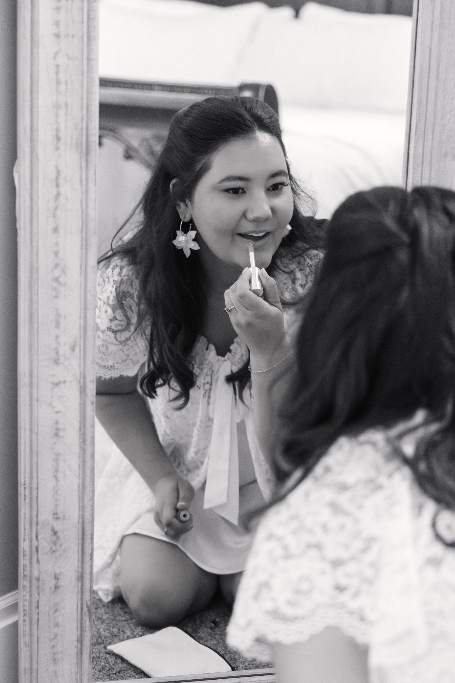 Black and white photo of bride applying lipstick while kneeling in front of a mirror.
