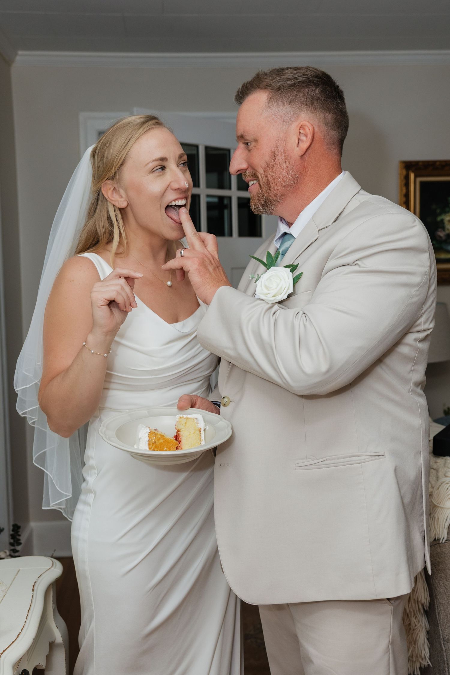 Bride and groom sharing wedding cake, groom feeding bride a bite while both smile joyfully in elegant attire.
