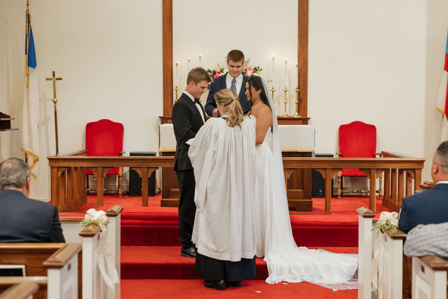 Bride and groom holding hands before officiant during intimate church wedding ceremony at the altar.