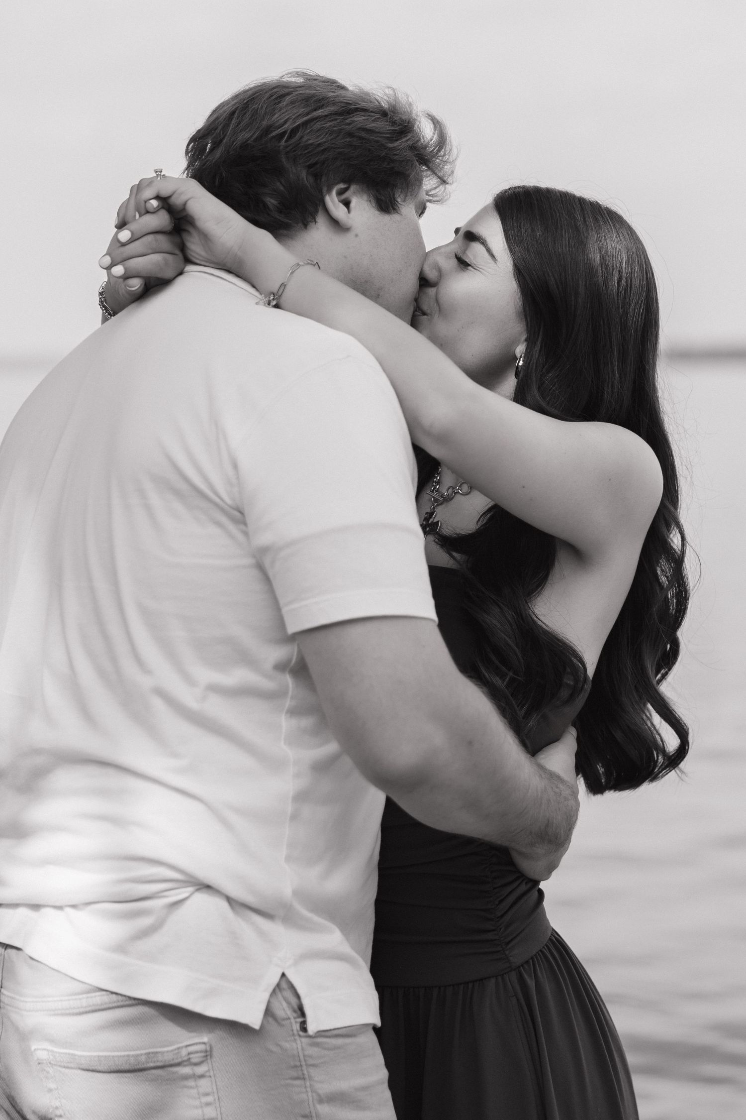 Black and white photo of couple sharing a passionate kiss by the lake.