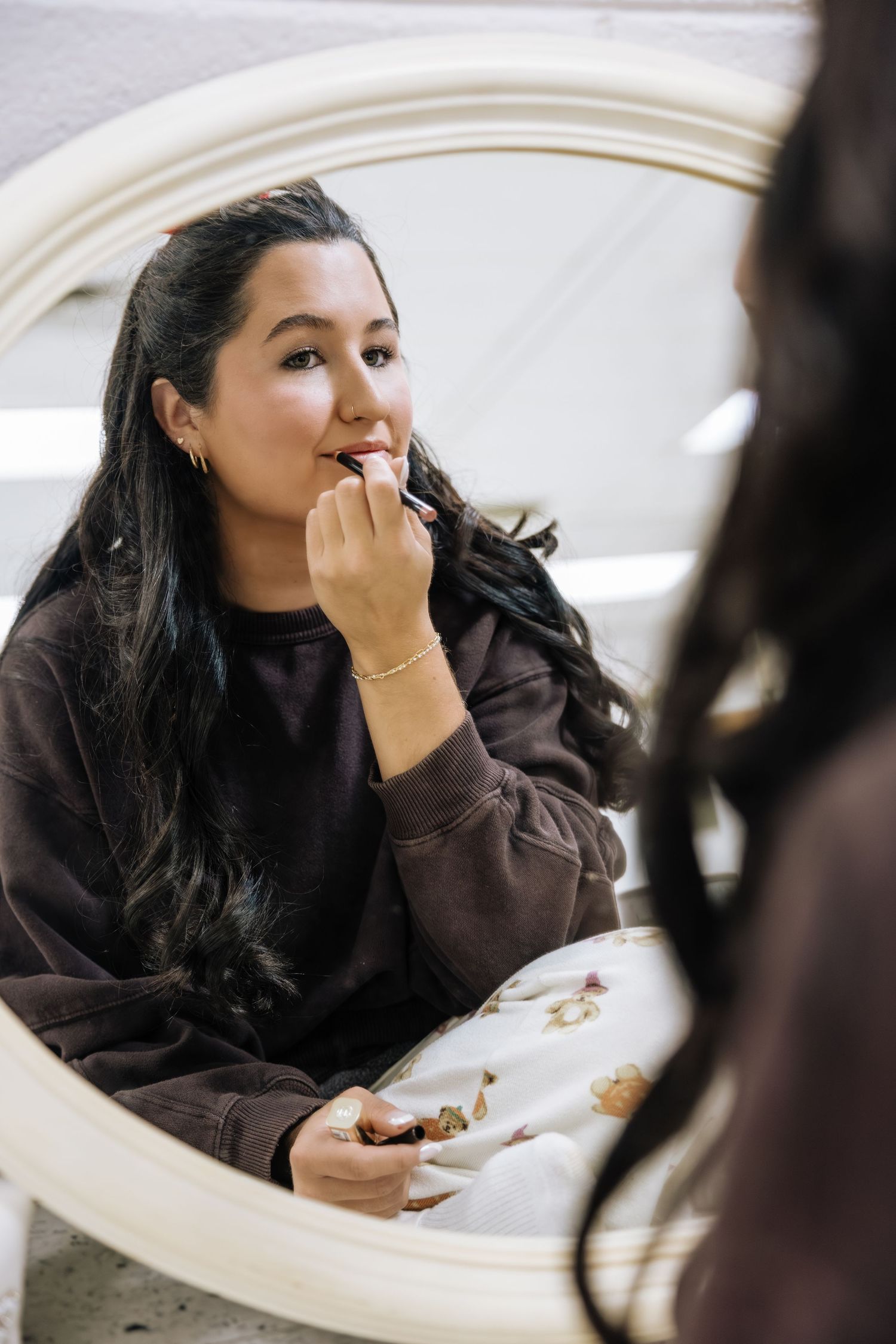 Young brunette bride doing makeup in round white mirror before wedding ceremony.