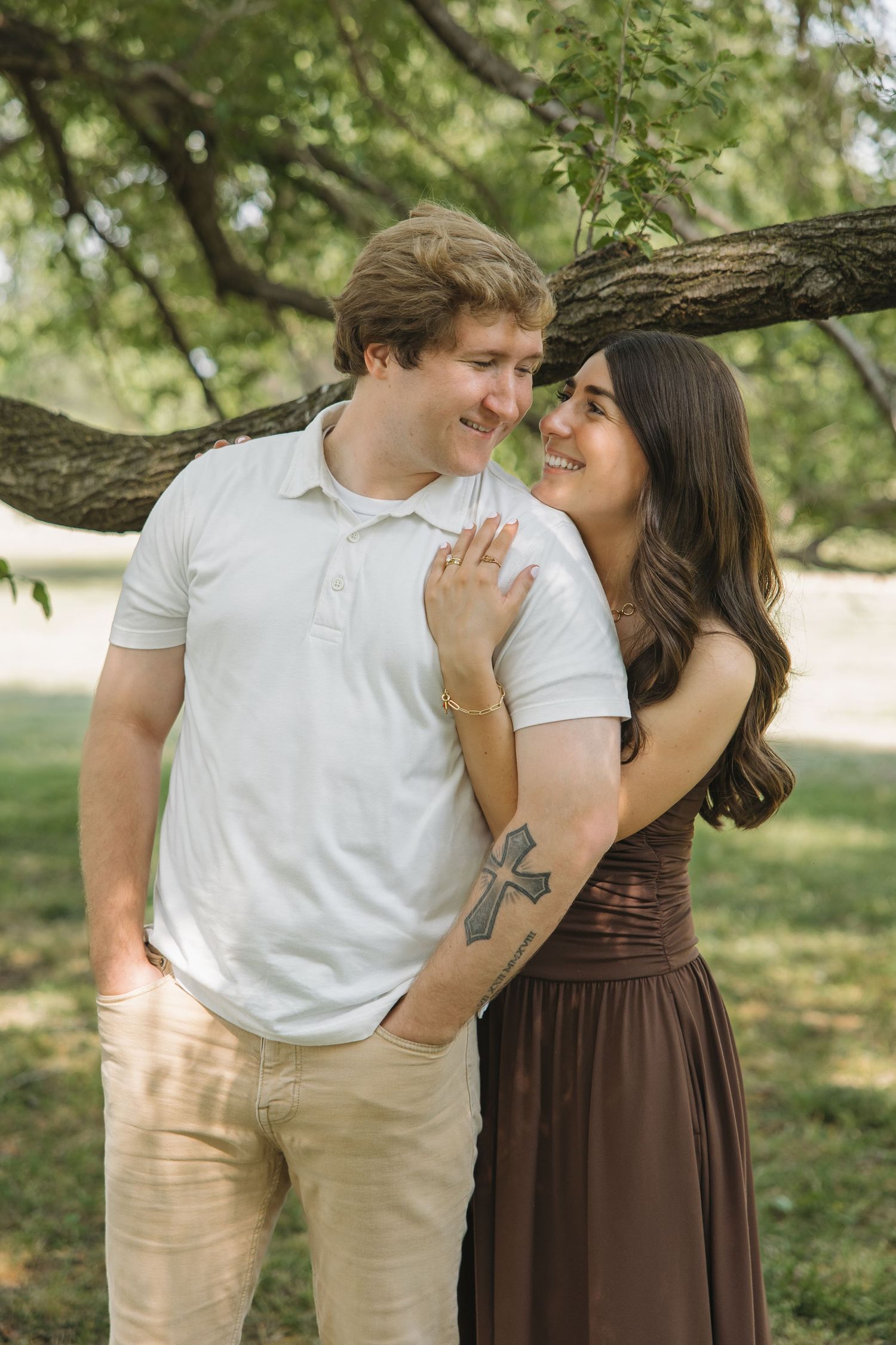 Couple smiling and leaning close together under a tree branch in a green park.