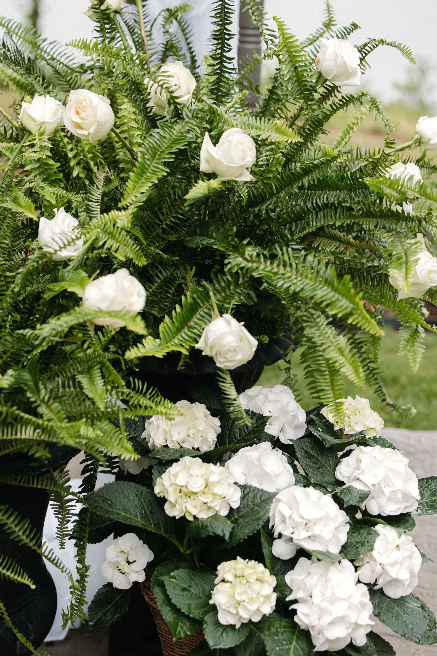 Elegant wedding floral arrangement featuring white roses, hydrangeas, and lush green ferns in a garden setting.
