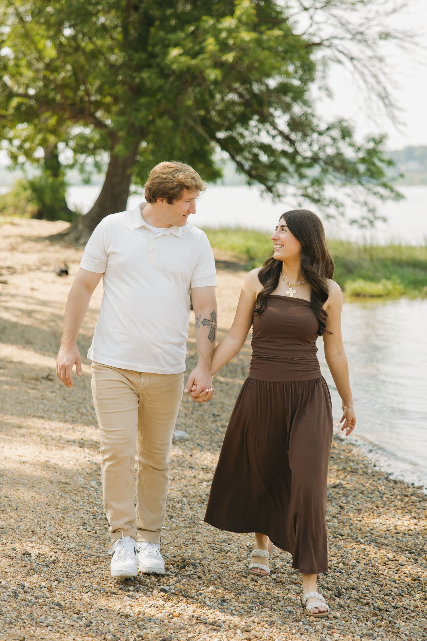 Happy couple walking hand in hand along a scenic lakeside pebble path.