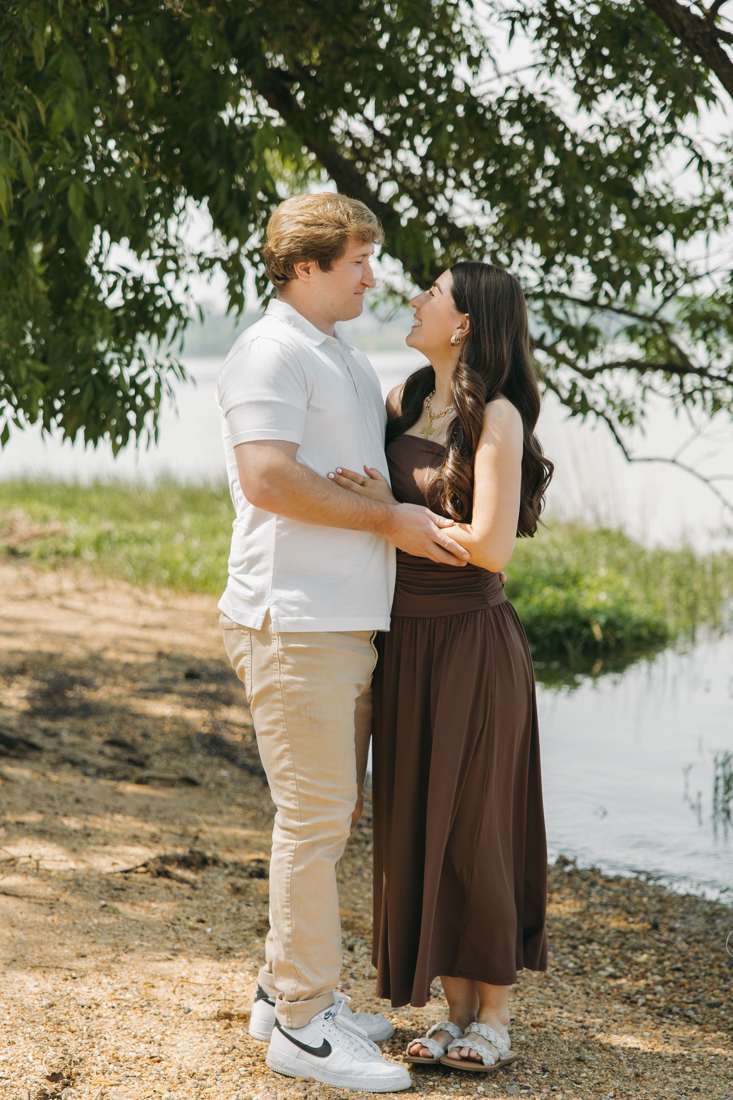 Romantic couple gazing into each other's eyes while embracing near a peaceful lakeside.