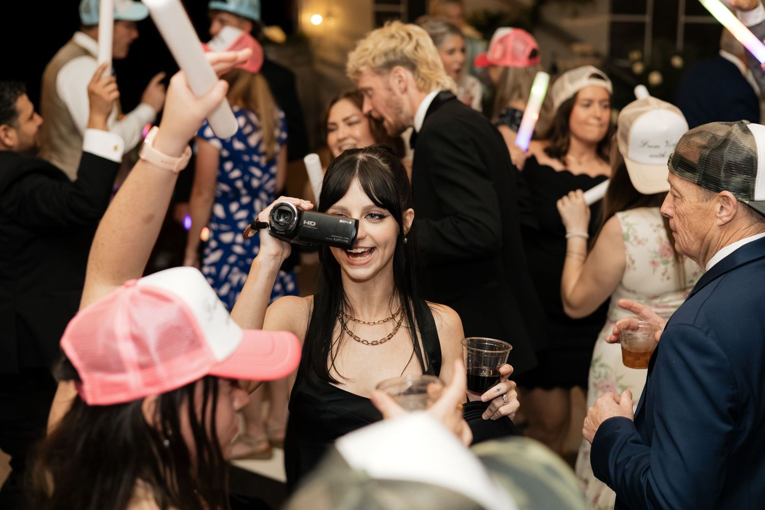Wedding guest smiling while holding a video camera at a festive reception party with glowing accessories.