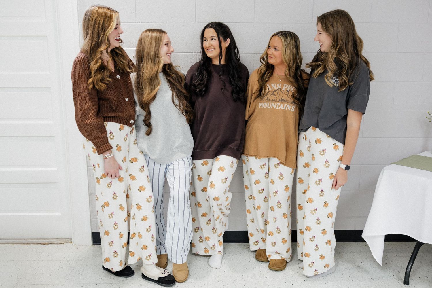 Five women in matching floral pajama pants laugh together in a candid group photo.