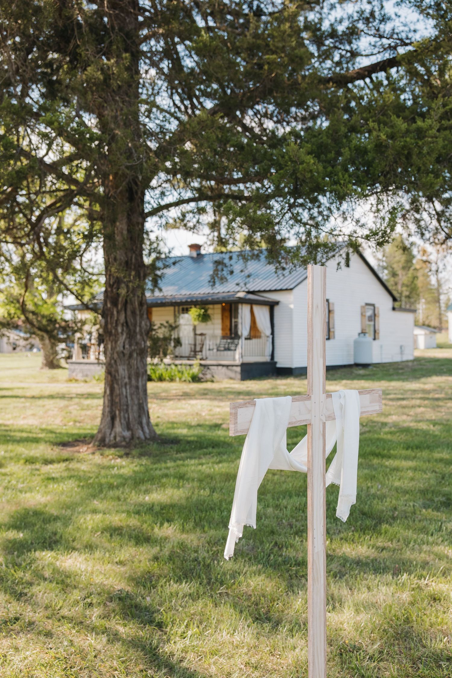 White wedding dress draped over wooden stand in green lawn with farmhouse background.