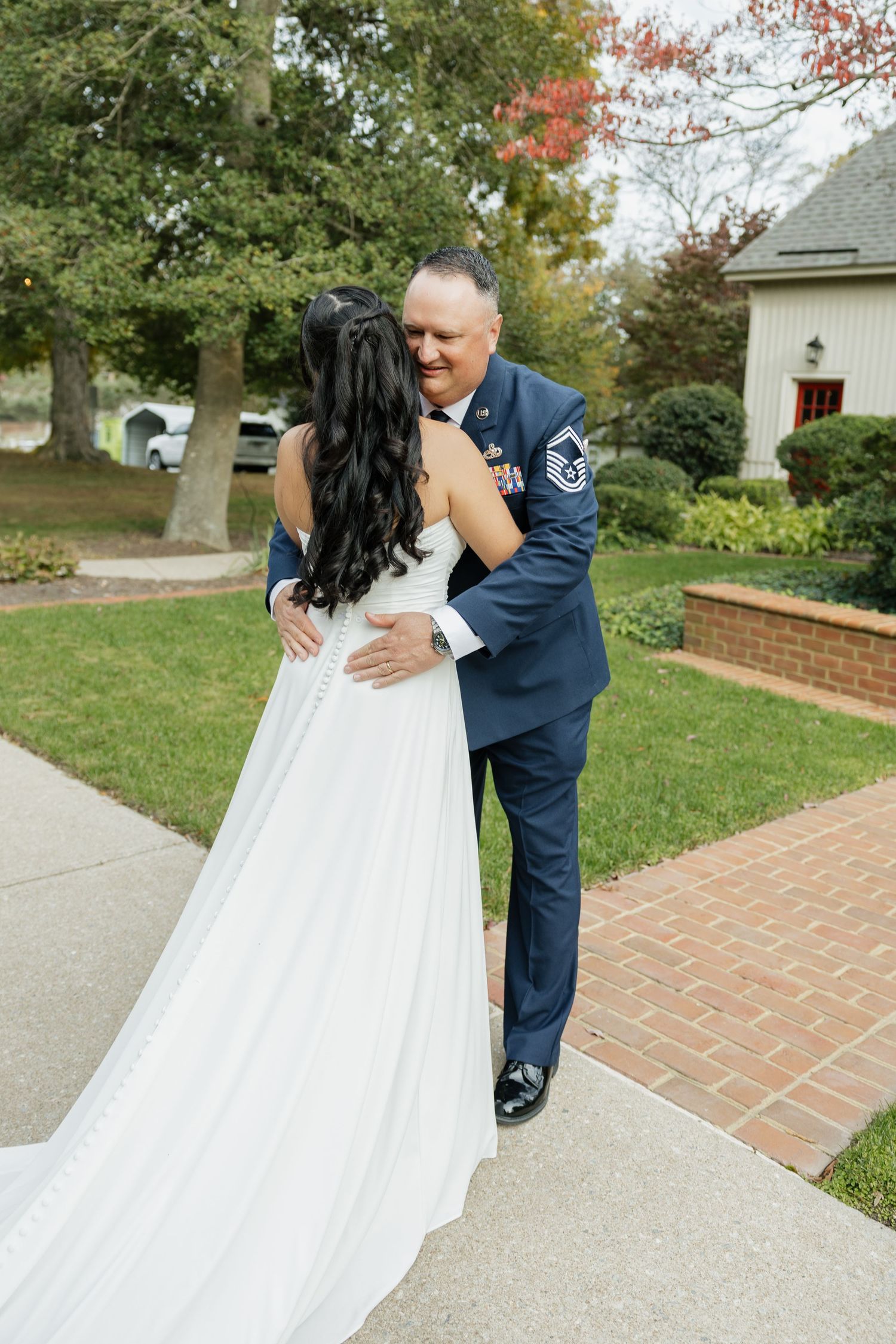 Military groom in blue uniform embracing bride in white gown during emotional first look outdoors.
