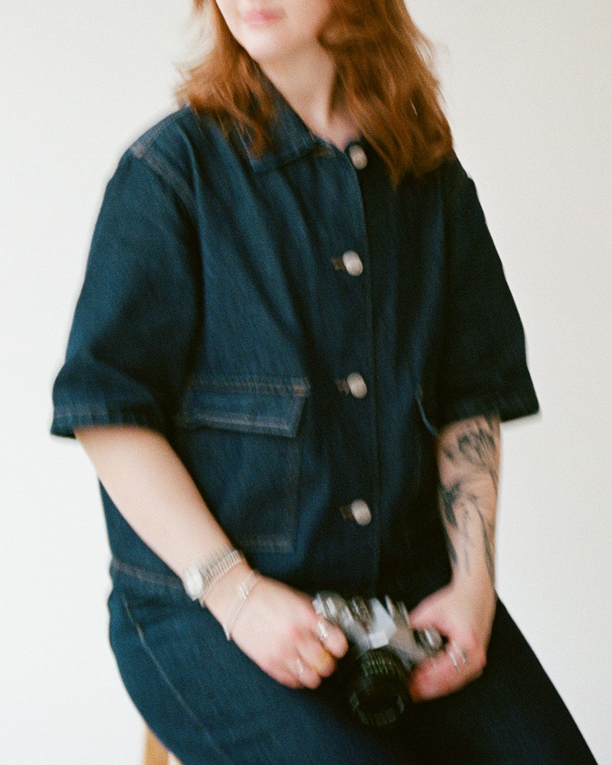 Photographer holding a film camera, wearing an all denim outfit, and the image is slightly blurred.