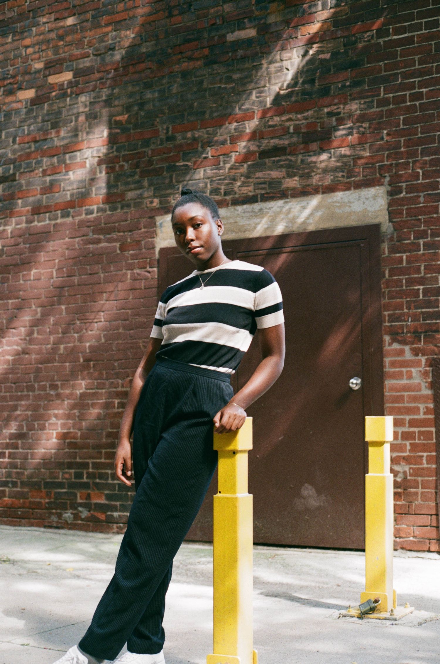 A woman wearing a black and white striped t-shirt and black pants posing in a brown brick alley in Downtown Toronto for film portraits.