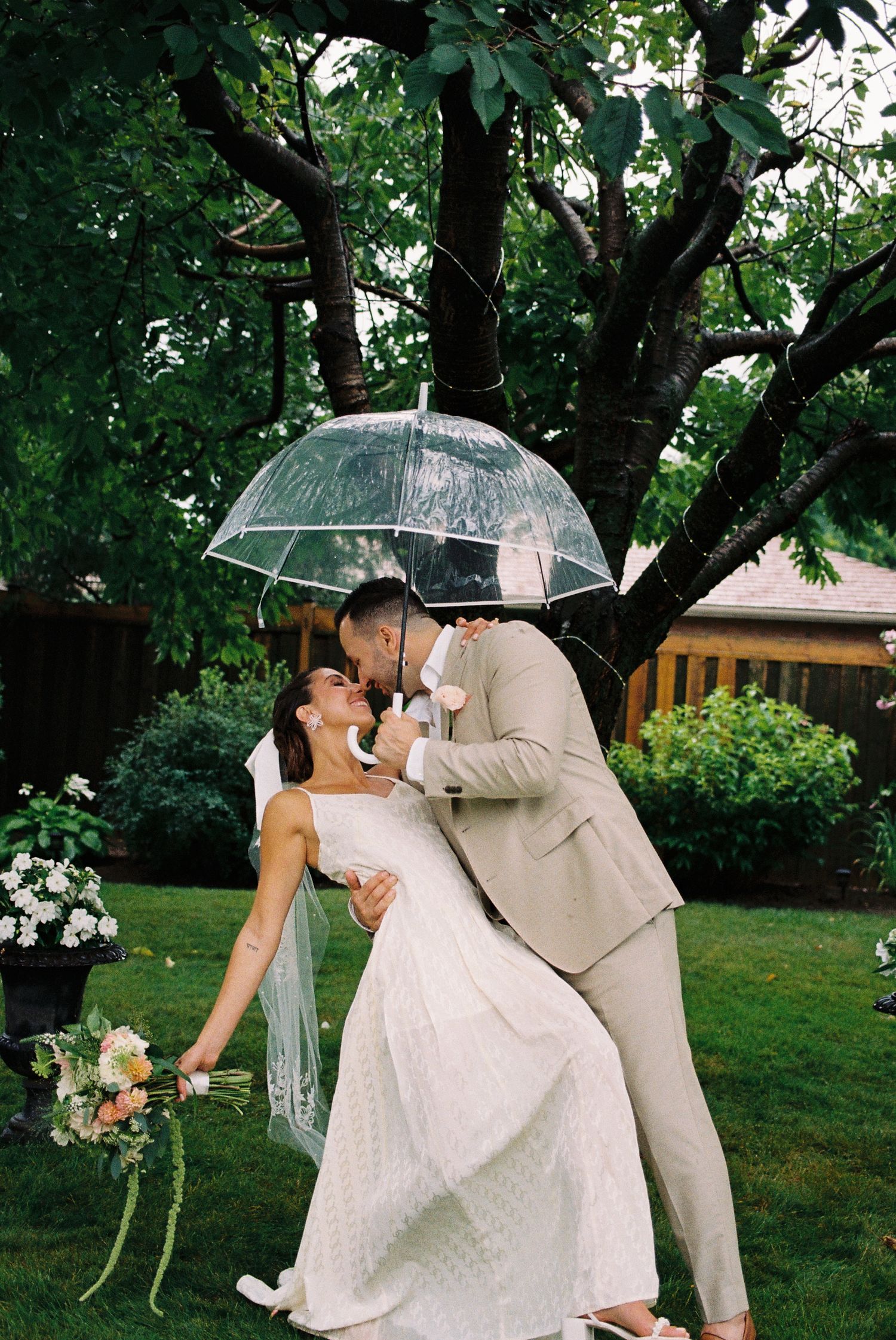Bride and groom underneath a clear umbrella in the rain.