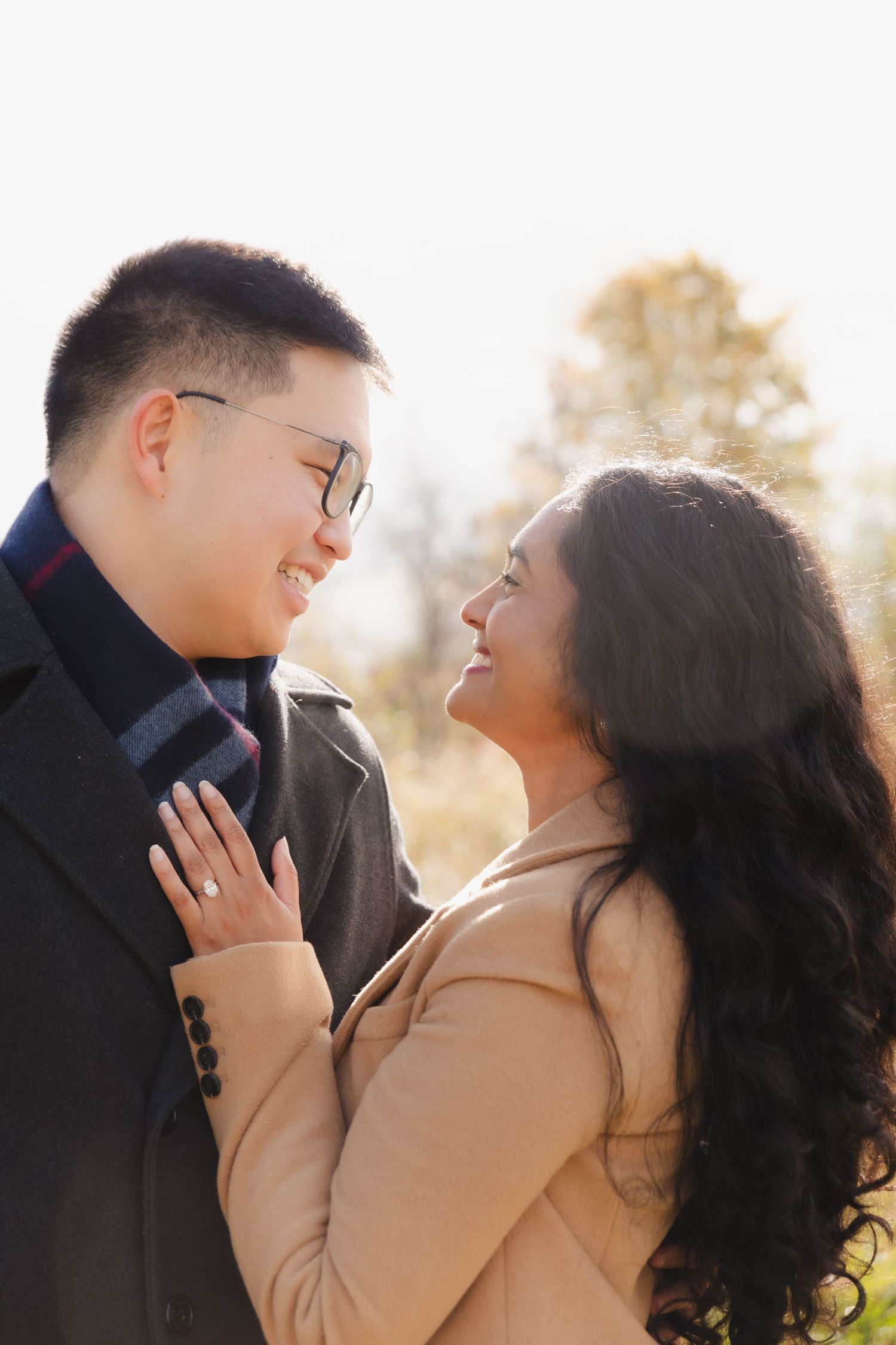 Fiancés smiling lovingly at each other. The woman rests her hand with her engagement ring on her partner's chest.