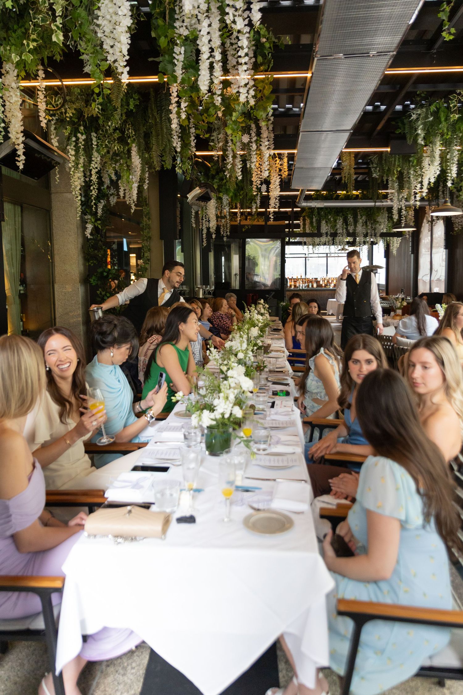 Bridal party sitting at bridal shower at Black & Blue Steakhouse in Toronto. The tables and ceiling are covered in green and white florals.