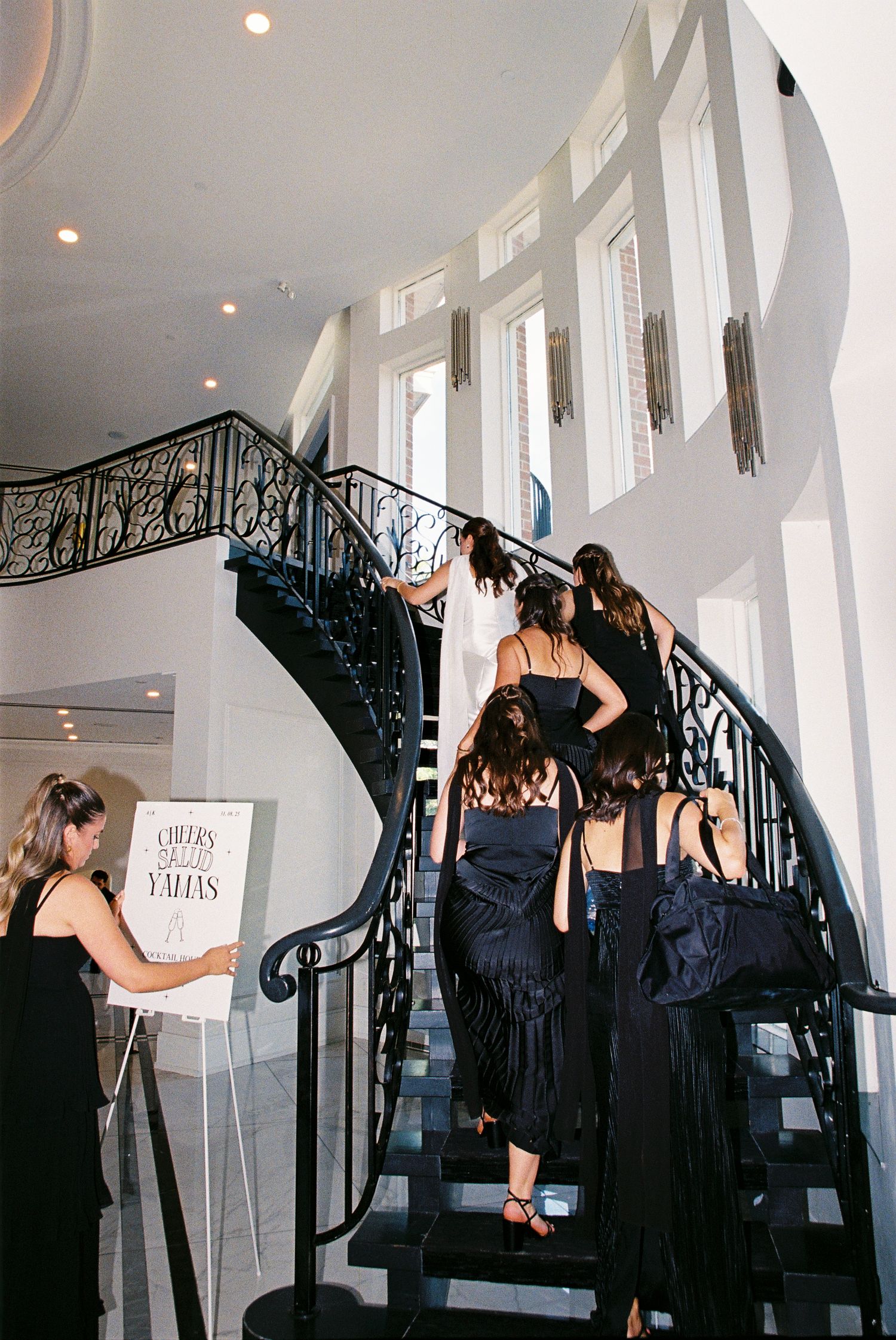 Bride and bridal party ascend a curved set of stairs to finish getting ready.