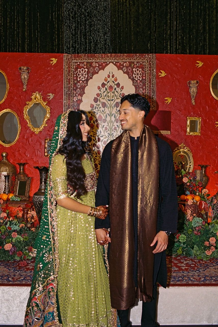 Bride and groom smiling at each other in front of an intricate red, floral backdrop.