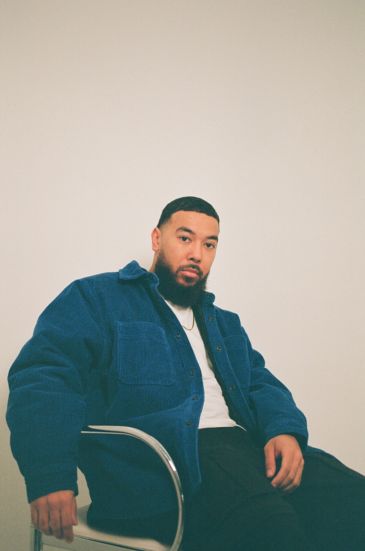 Film portrait of man sitting in a chair wearing a blue jacket.