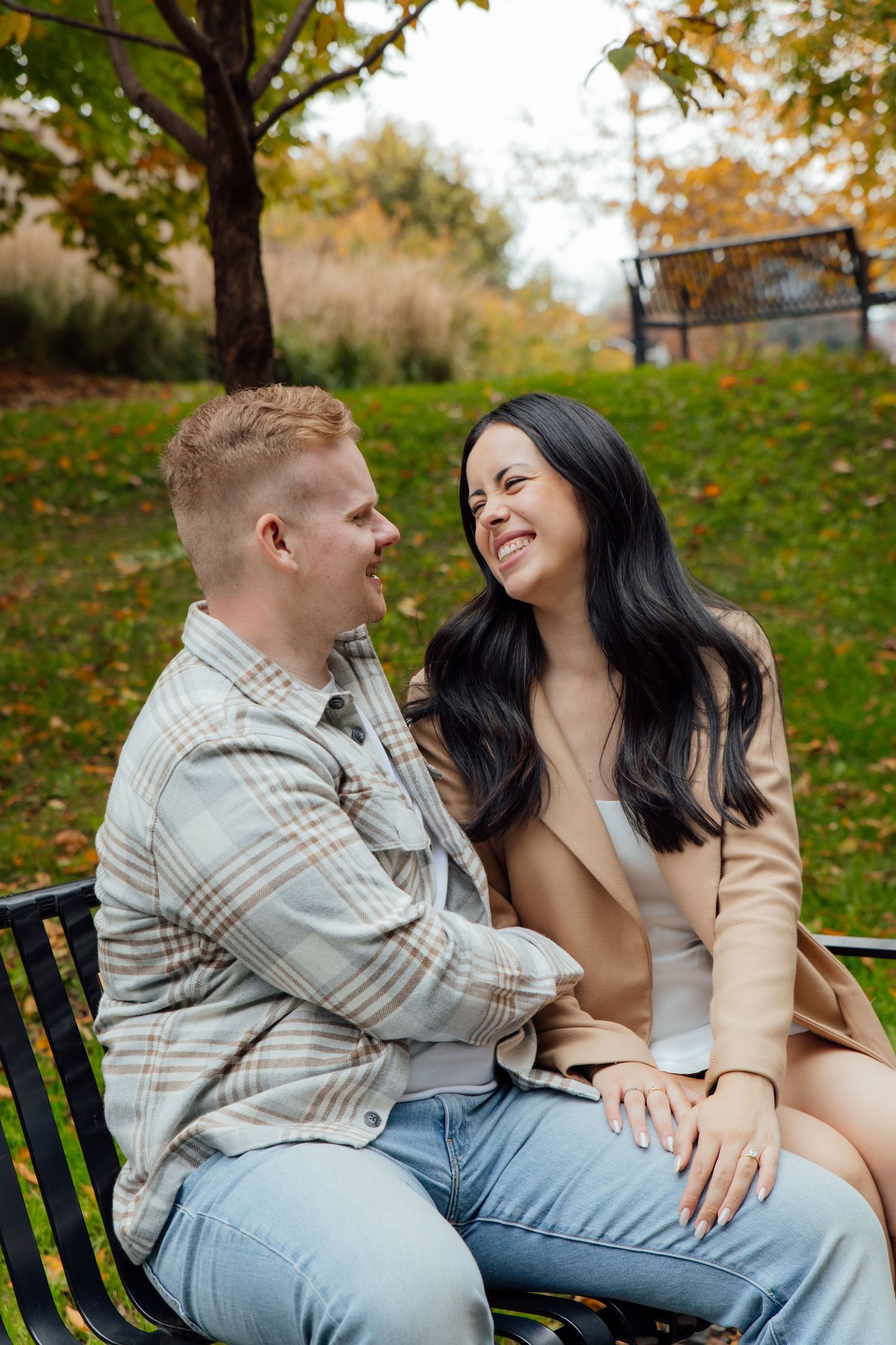 Fiancés holding hands and sitting on a park bench while smiling and looking into each other's eyes.