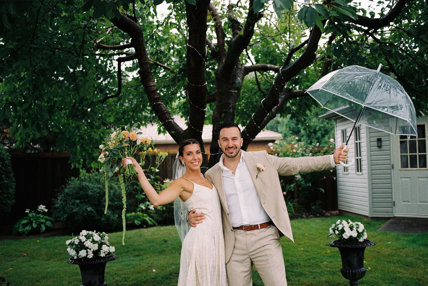 Bride and groom underneath a clear umbrella in the rain.