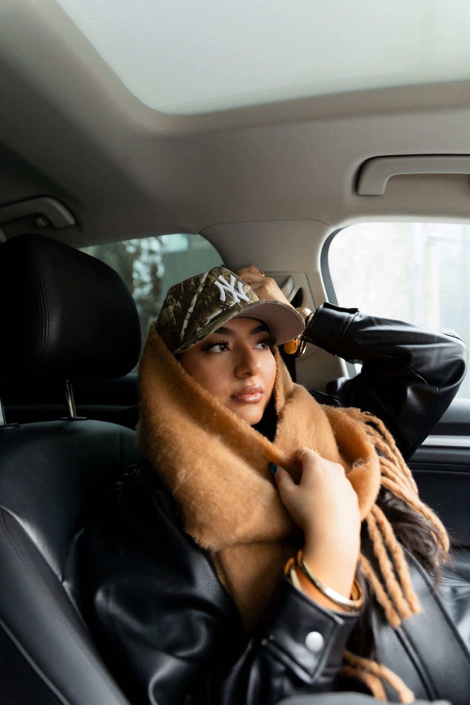Woman posed in a car wearing a brown scarf and camo hat.