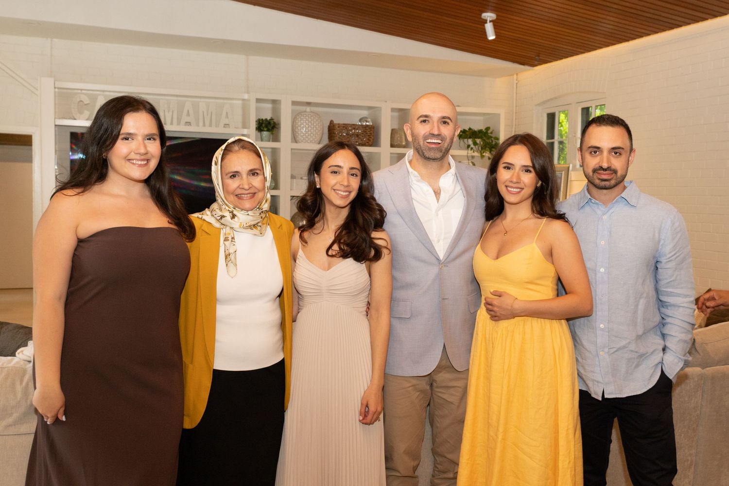 Six people—bride, groom, two sisters, one brother, and one mother of the bride—are posed together for a family photo at an engagement party