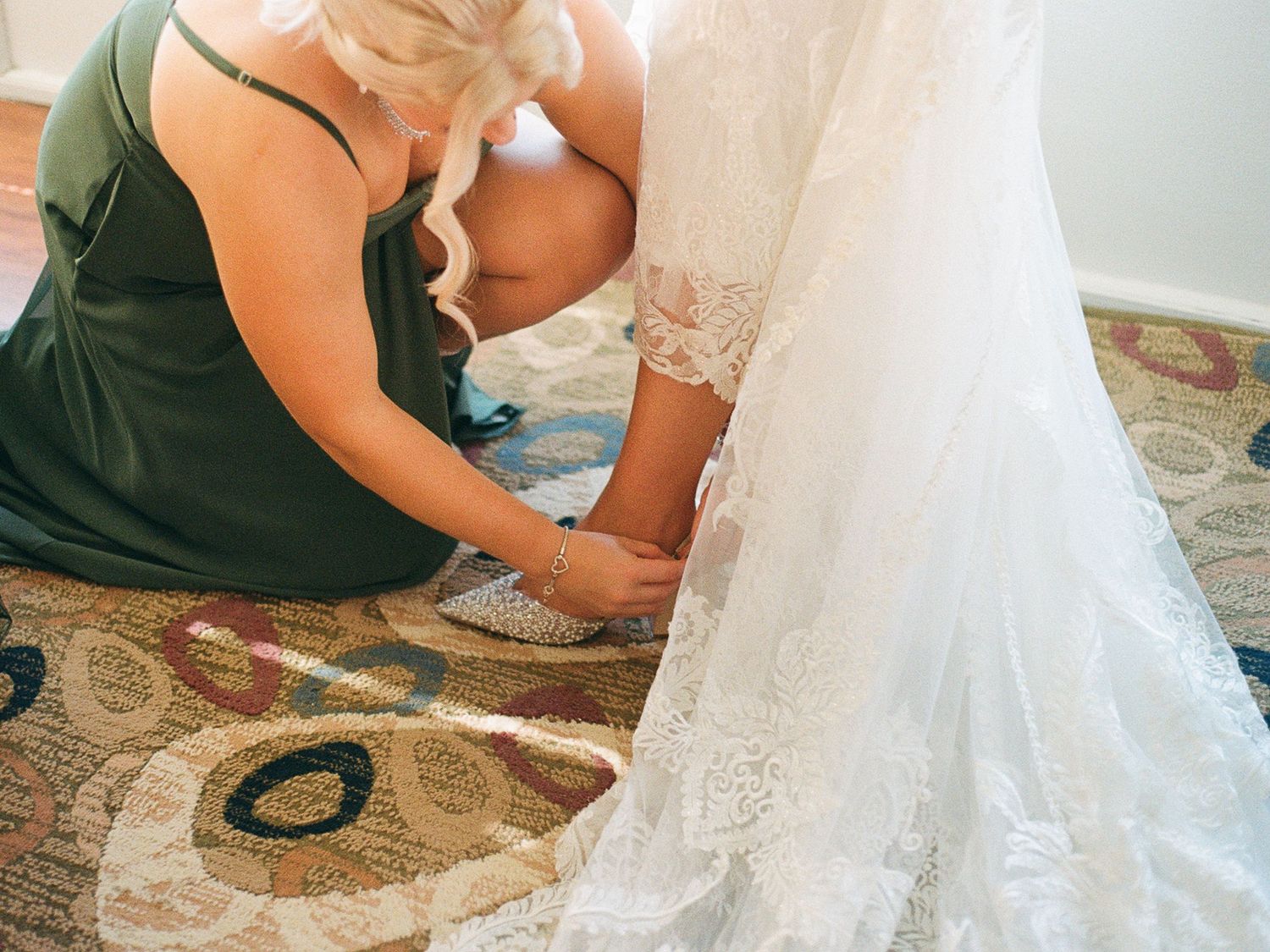 Film photo of a maid of honour helping bride get ready by lacing up her high heel on her wedding day.