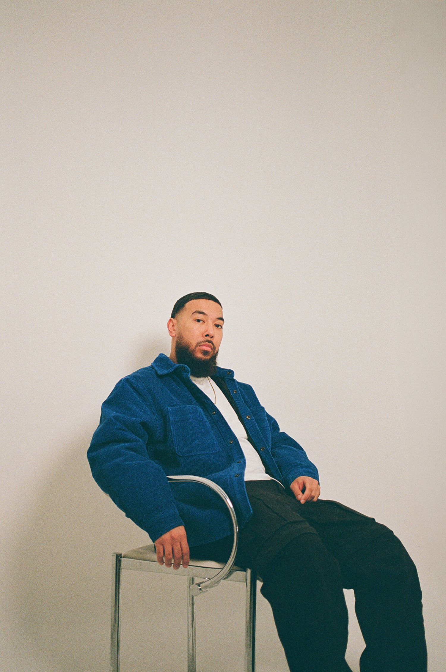 Film portrait of man sitting in a chair wearing a blue jacket.