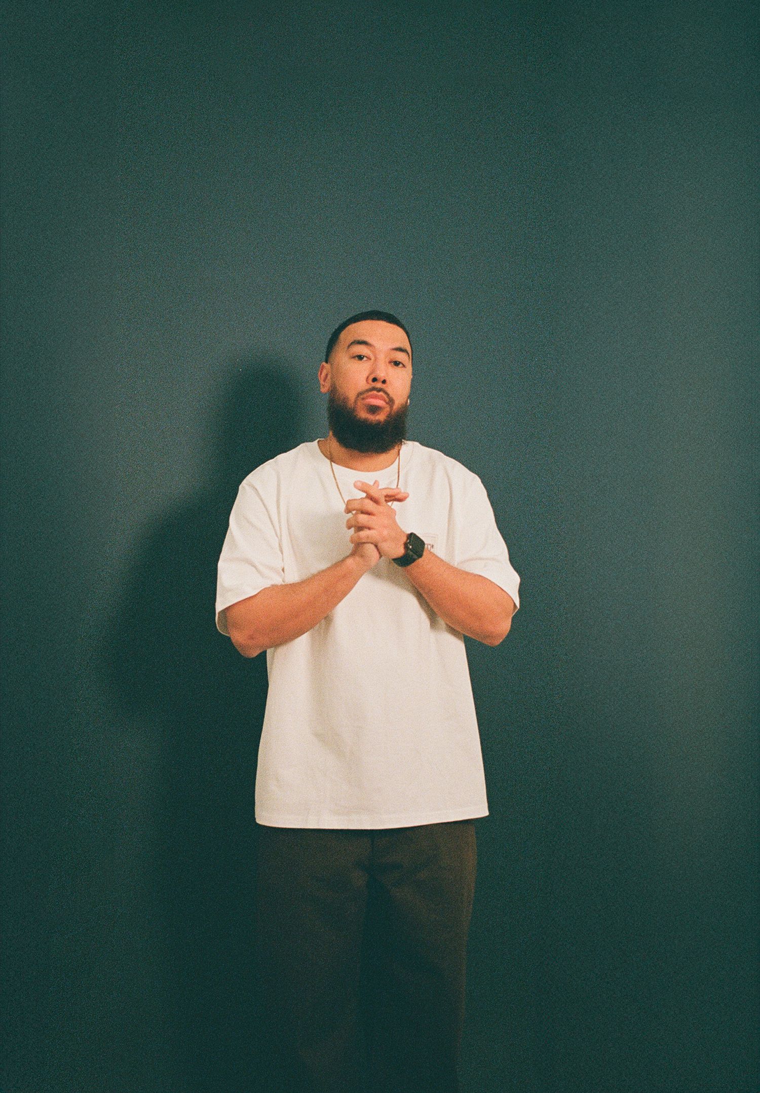 A man wearing a white t-shirt poses for a film photo in front of a teal coloured studio backdrop.