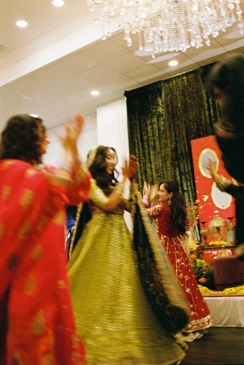 Bride and her bridesmaids dancing together, captured on film. There is a slight motion blur from their movement.