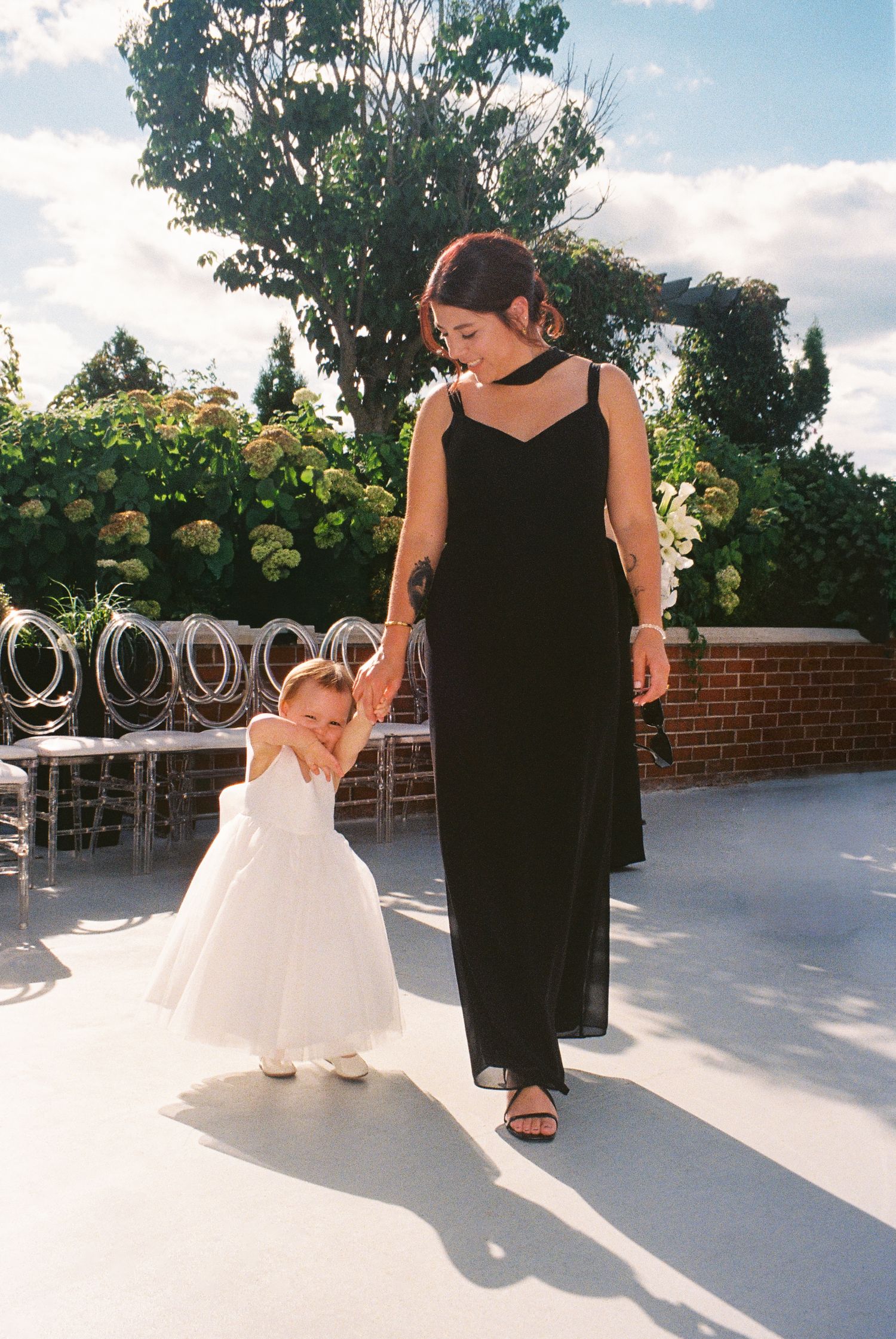 Bridesmaid walks with flower girl who shies away from the camera.