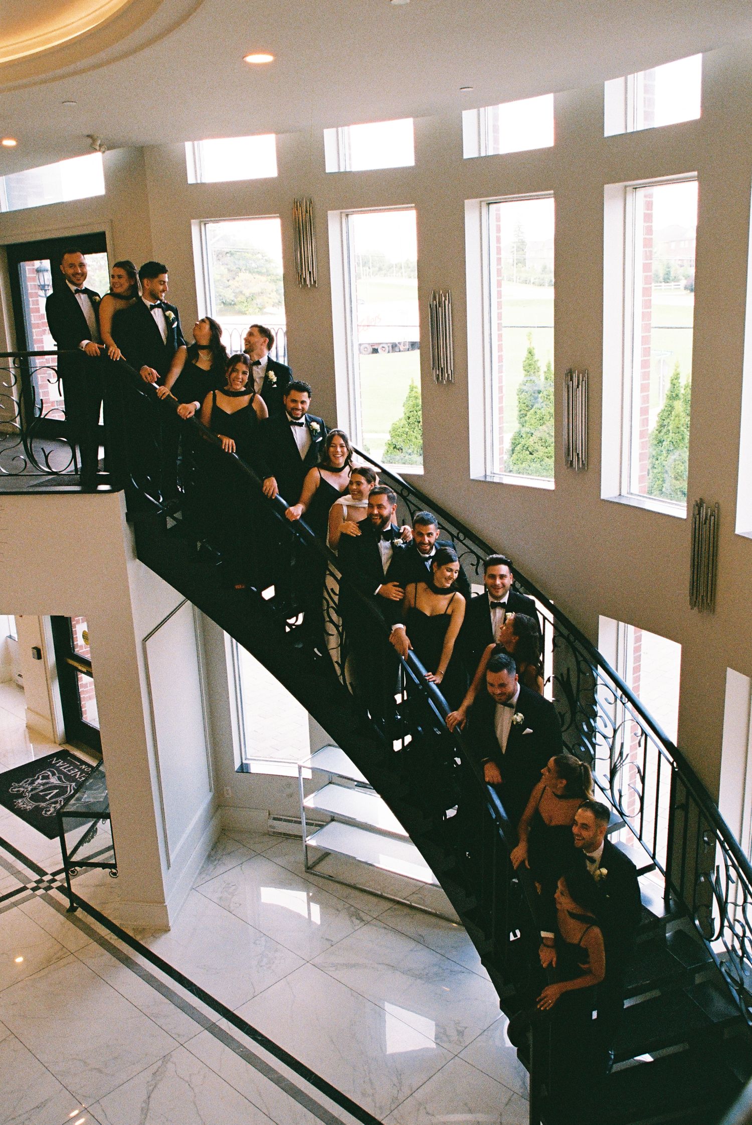 Bride, groom, bridal party, and groomsmen stand together on a grand staircase at the Royal Venetian Mansion in Vaughan, Ontario.