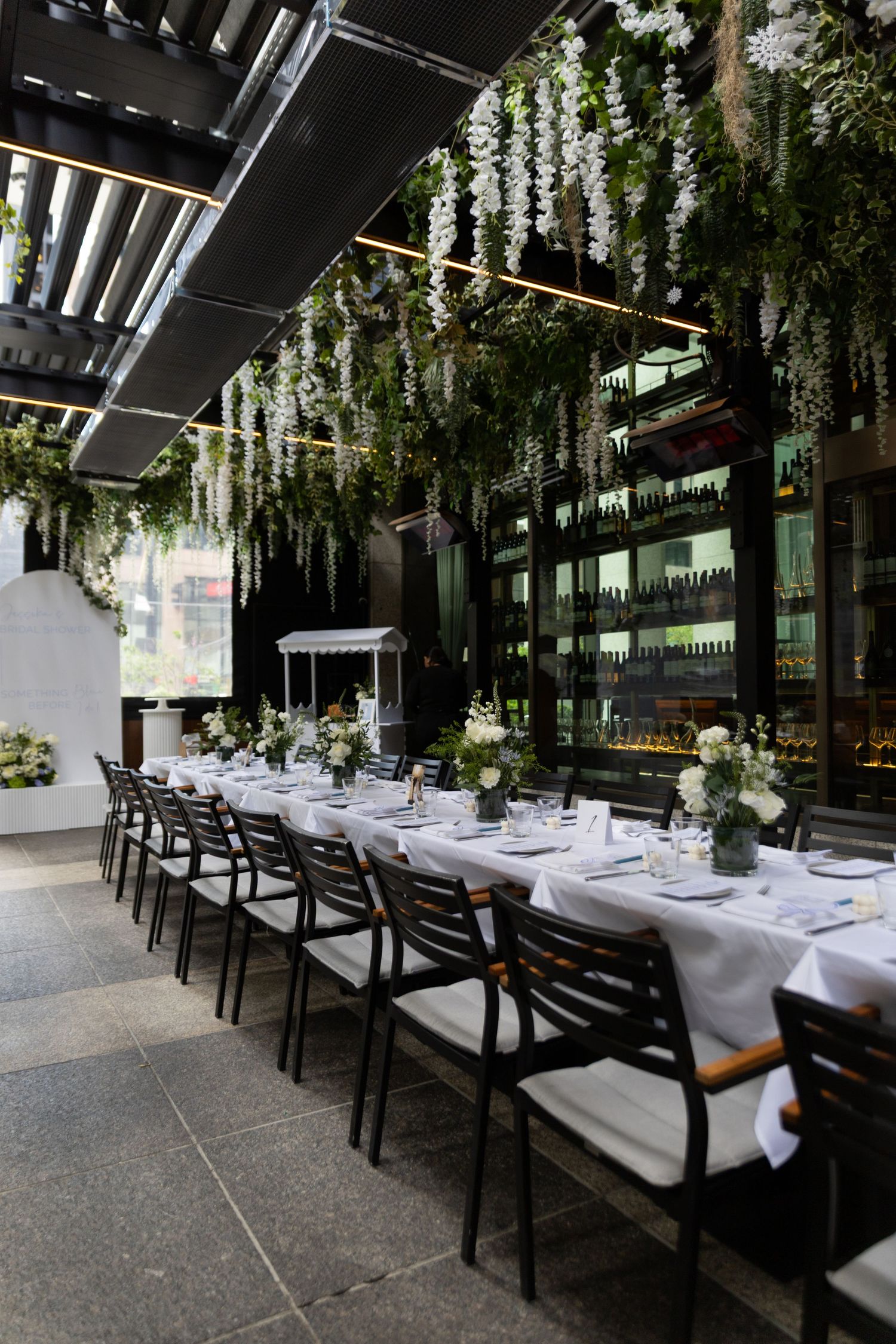 Event photo of white table, black chairs, and floral and greenery decor set up at bridal shower.