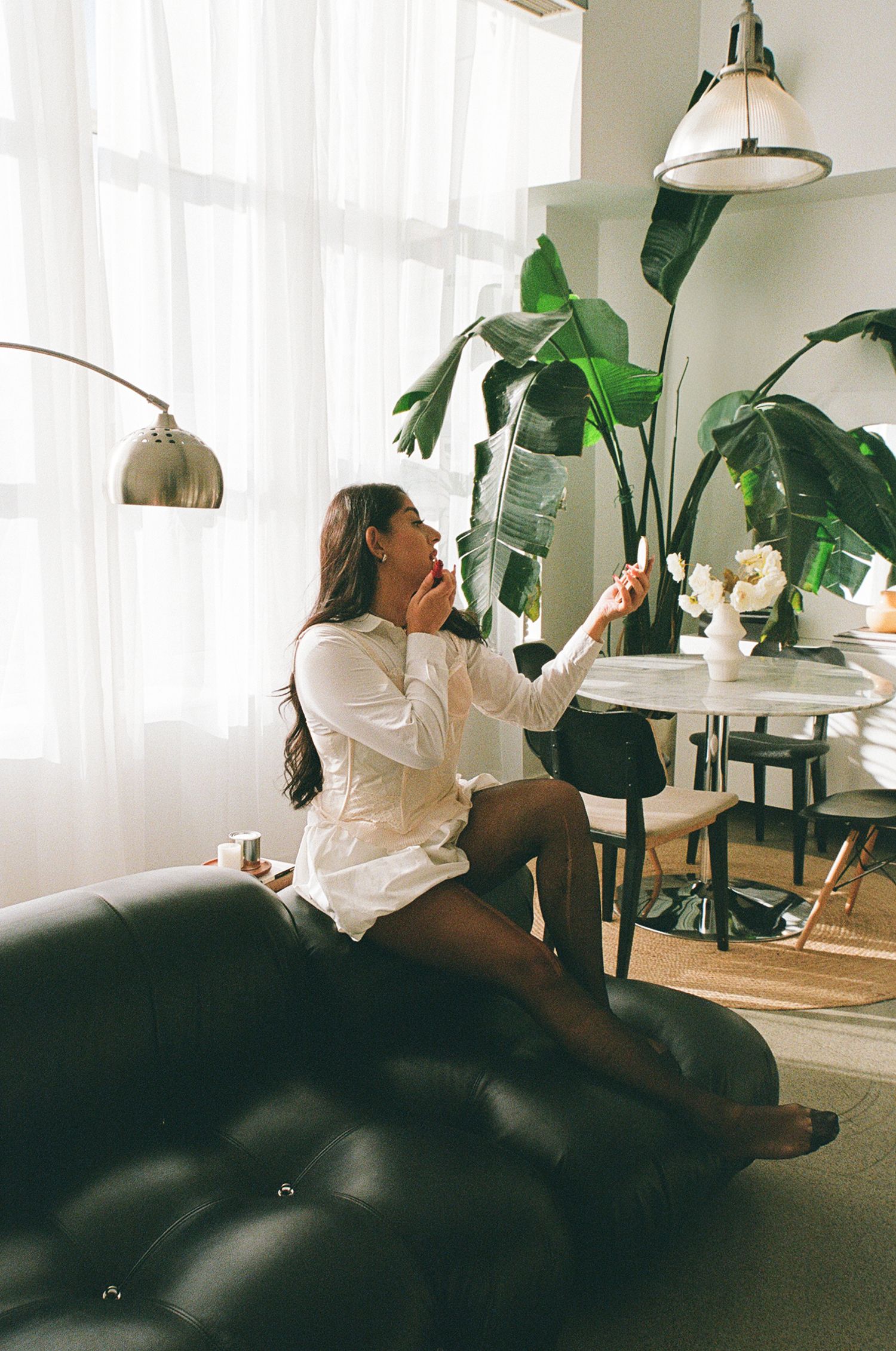 Woman sitting on a black leather couch applying makeup.