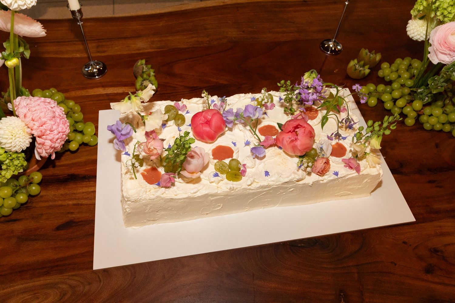 White cake with green, pink, and light purple coloured florals at an engagement party.